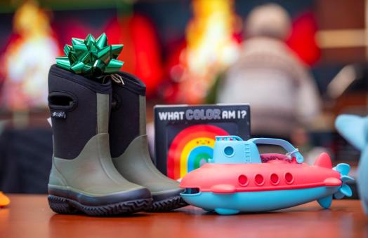 A photo of a pair of rainboots and toys sitting on a table waiting to be wrapped into Winter Wishes gifts. 