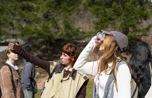 one student points stright ahead and another looks toward the sky through a device