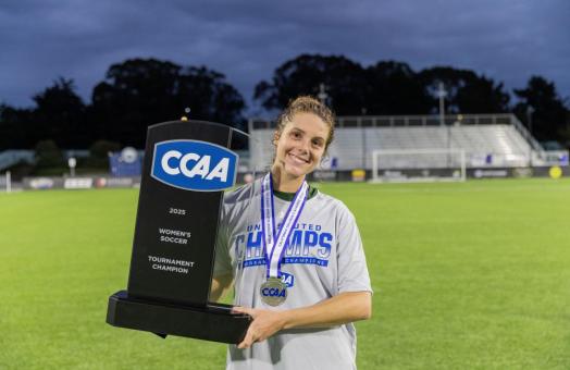 A photo of Cal Poly Humboldt women's soccer player Josie Wolitzky holding the CCAA Women's Tournament trophy. 
