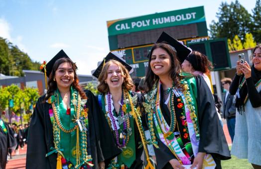 A photo of three grads at spring Commencement in the redwood bowl. 