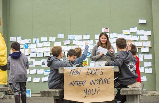 children sitting at a bench with a sign attached to it that reads, "how does water inspire you?"