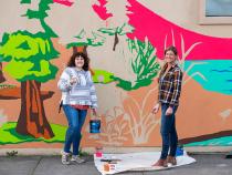 Caroline Voorhees (left), student teacher and Art Education alumna, and Redwood Coast Montessori High School art teacher Saha Lyth (left), working on the school mural.
