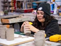 A photo of a student sponging clay mugs to be identical.