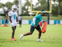 A photo of Robert Prince running with a football pylon and a Miami Dolphins player in full practice gear during a training session.