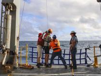 Claire and Ralph (left) work with the marine technicians (right) to attach a GoFlo bottle to the line just before deploying it. It will go down into the water open, and they will trigger it to close at the depth they want. Photo from Karina Vivanco.